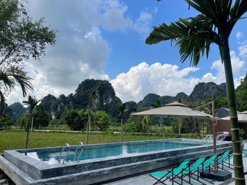 a swimming pool with chairs and an umbrella and mountains at Ninh Binh Mountainside Bungalow in Ninh Binh