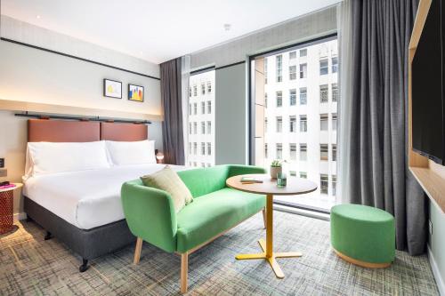 a hotel room with a bed and a green couch at Holiday Inn Melbourne Bourke Street Mall by IHG in Melbourne