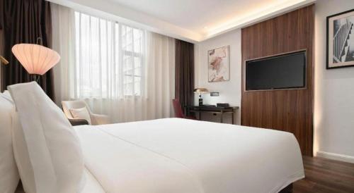 a hotel room with a white bed and a television at Jinjiang Metropolo Haikou East High Speed Railway Station Normal University in Haikou