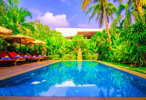 a pool with chairs and umbrellas next to a resort at Angkor Land House in Phumĭ Réach Born