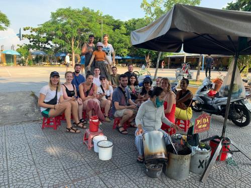 a group of people sitting in chairs under an umbrella at Cheerful Hoi An Hostel in Hoi An