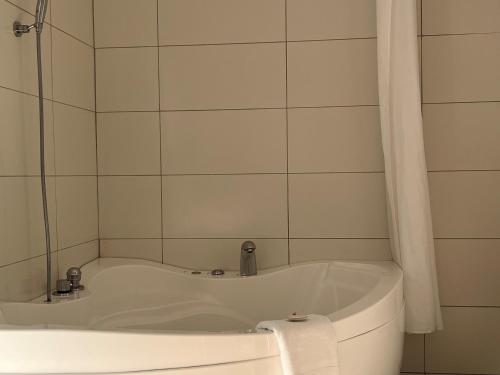 a white bath tub in a white tiled bathroom at Airport Manor Inn in Auckland