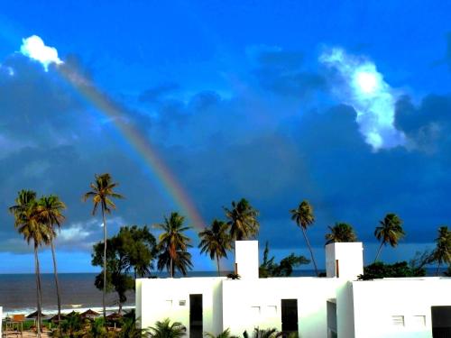 a rainbow over a white building with palm trees at B Blue Beachouses in Itacimirim
