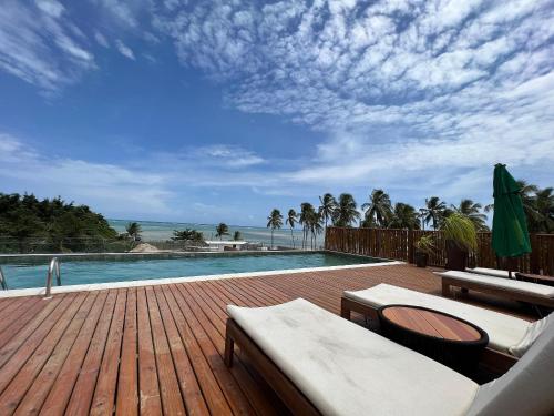 a wooden deck with a pool and chairs at Beira mar porto de pedras essence C101 in Pôrto de Pedras