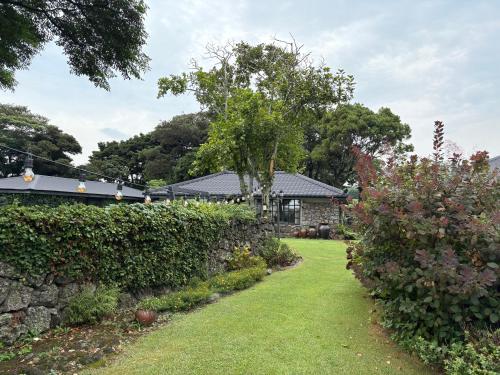 a garden with a stone wall and some bushes at Imjingotaek Hanok Stay Jeju Traditional House LP Cozy House, Wagon stay at Imjingotaek in Jeju