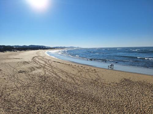 two people walking on a sandy beach near the ocean at Seaside Beach House with Pool & Invertor in Port Alfred