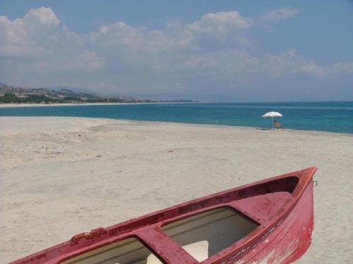 a red boat sitting on a beach with an umbrella at Ancient holiday home in the countryside of Stilo with garden in Guardavalle