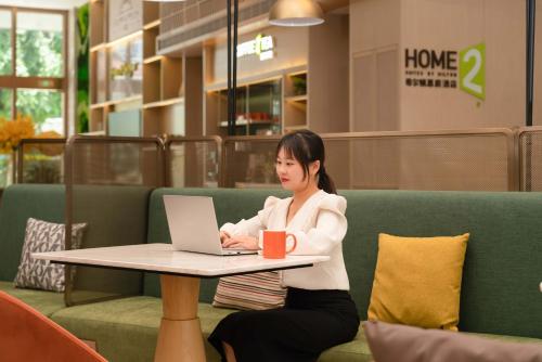 a woman sitting at a table with a laptop computer at Home2 Suite by Hilton Xishuangbanna Jinghong in Jinghong