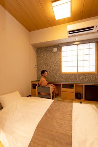 a woman sitting at a desk in a room with two beds at Hotel Matsunoi Shurin in Tokyo