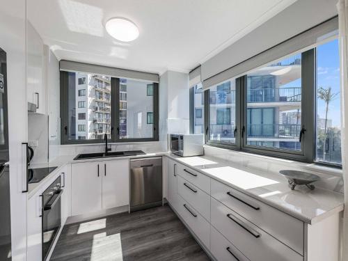 a kitchen with white cabinets and large windows at Meridian Alex Beach Apartments in Alexandra Headland