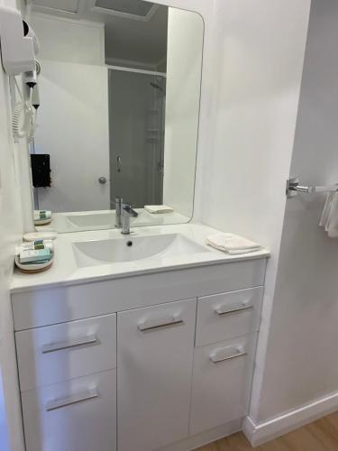a white bathroom with a sink and a mirror at Cascades Motor Lodge in Auckland
