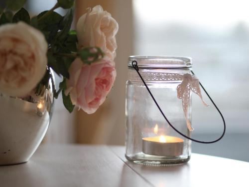 a candle in a glass jar next to a vase with flowers at Apartment in Glücksburg near Seabeach in Ulstrupfeld
