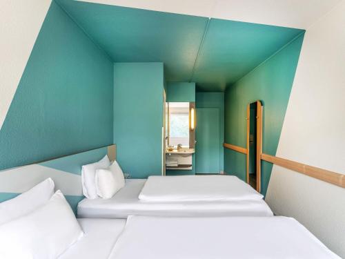 two beds in a room with a blue wall at B&B HOTEL Freiburg-West in Freiburg im Breisgau