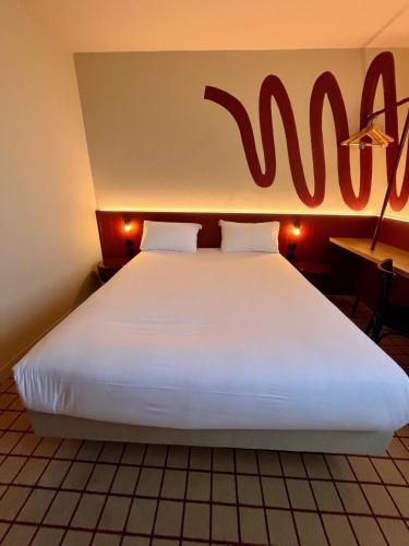 a large white bed in a room with a sign on the wall at The Originals City, Hôtel du Phare, Bordeaux Mérignac in Mérignac
