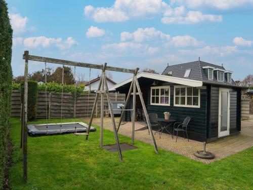 a small house with a swing set in the yard at Holiday Home Egmond near Dune Beaches in Egmond-Binnen