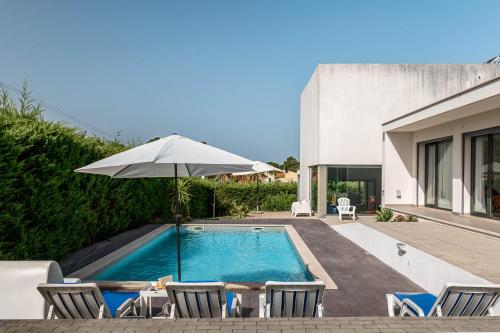 a pool with chairs and an umbrella next to a house at Sesimbra Villa with Private Pool and Garden - Total Privacy in Sesimbra