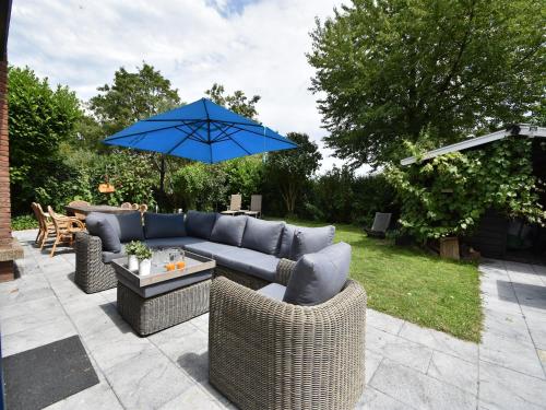 a patio with a couch and a blue umbrella at Villa in Bruinisse near Grevelingenmeer in Bruinisse