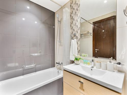 un bagno con vasca, lavandino e specchio di Savis Homes - Furnished Spacious Studio in Golf Promenade 2A by Damac Hills a Dubai