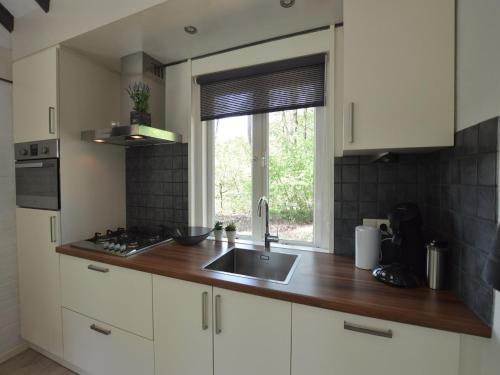 een keuken met witte kasten, een gootsteen en een raam bij Romantic Forest Retreat with Sauna in Stramproy