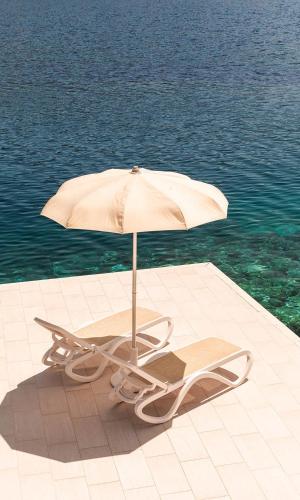 a chair and an umbrella on a patio next to the water at Aminess Younique Lume Hotel in Brna