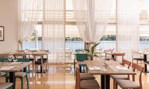 a restaurant with tables and chairs and windows at Aminess Younique Lume Hotel in Brna