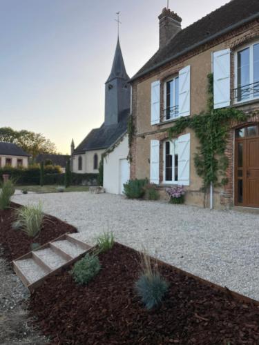 une maison avec une allée en gravier et une église dans l'établissement Le Presbytère, maison de campagne familiale, à La Poterie-au-Perche