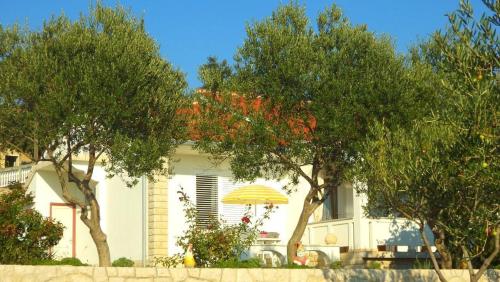 a white house with a yellow umbrella and trees at Appartement In Kampor in Rab