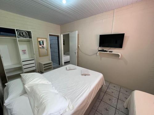 a bedroom with a white bed and a flat screen tv at Recanto Armação Pousada in Penha