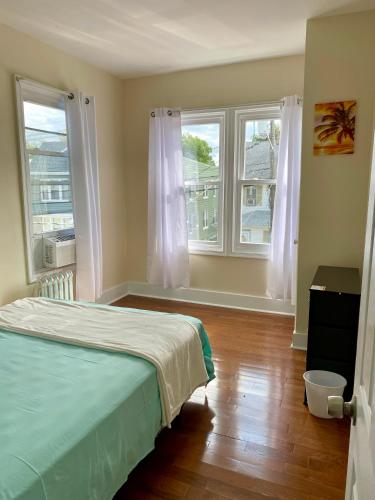 a bedroom with two windows and a bed and wooden floors at Tropical Oasis - Room 1 in Irvington