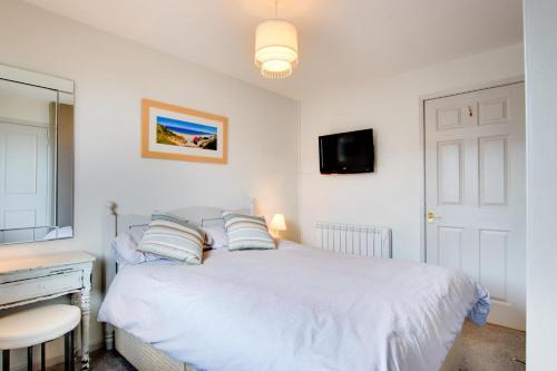 a bedroom with a white bed with a desk and a television at Kookaburra in Abersoch
