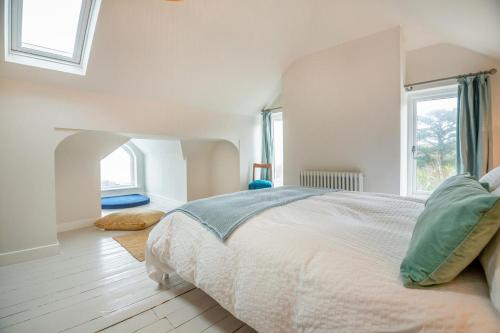 a white bedroom with a bed and two windows at Hywelfa in Abersoch