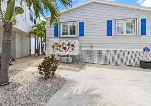 a white house with blue shutters and a palm tree at Oceanview Retreat with 60ft Seawall in Cudjoe Key