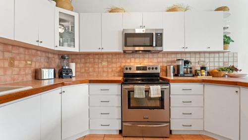 a kitchen with white cabinets and a stove and microwave at Beachfront Surf House-Family Fun, Pool and Solar in Rincon