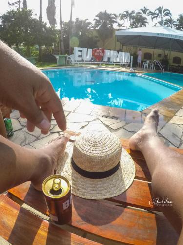 a person holding a straw hat on a table next to a pool at Pousada Cabo Frio in Cabo Frio