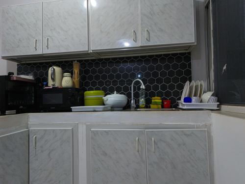 a kitchen with white cabinets and a black tiled wall at Beachfront Bliss Zanzibar - Stylish 1BR Oceanview Apartment in Uroa in Uroa