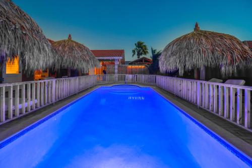 a swimming pool with two thatched umbrellas at Moderne Studio Sea dichtbij de zee met zwembad in Oranjestad