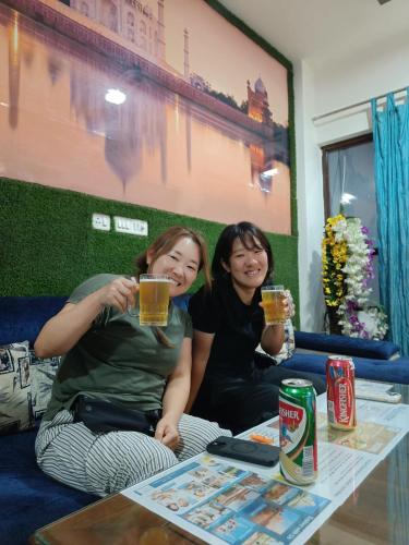 two women sitting on a couch holding glasses of beer at The Hideout Agra - Garden Homestay near Taj in Agra
