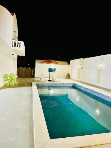 a swimming pool with an umbrella and a table and chairs at Villa Soltana in Zarzis