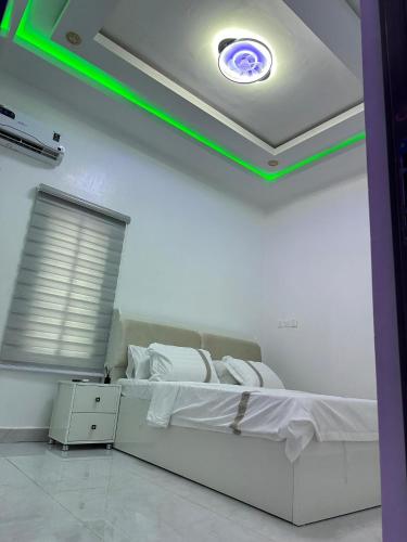 Un dormitorio con una cama blanca con una luz verde. en SG Apartments, en Abuja