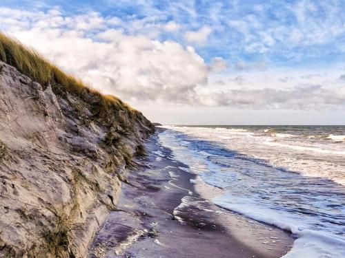 a sandy beach next to the ocean on a cloudy day at 2 person holiday home in Højer in Højer