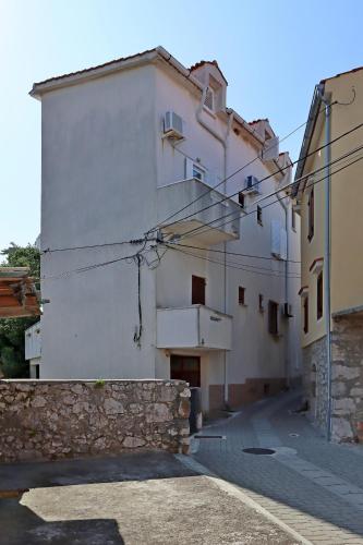 a white building with a stone wall next to a street at Apartments and rooms with parking space Vrbnik, Krk - 5302 in Vrbnik