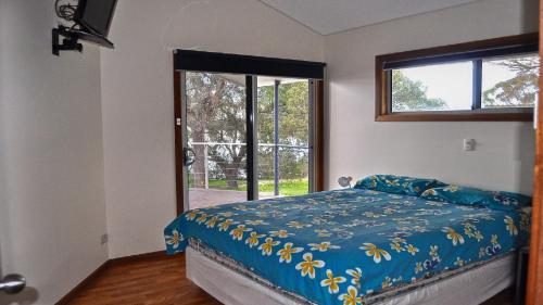 a bedroom with a bed with a blue comforter and a window at Rest A Shore Coffin Bay in Coffin Bay