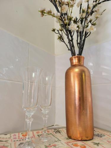 a bronze vase with flowers and two glasses on a table at Corella Accommodation 1C, everything you need in Boulder