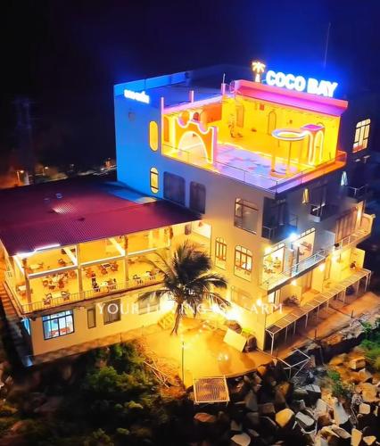 a lit up building with a palm tree in front of it at Coco Bay Hon Son in Lai Sơn