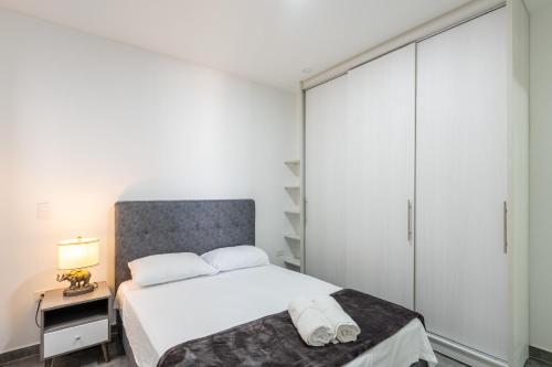 a white bedroom with a bed and a night stand at Apartahotelquimbaya in Quimbaya