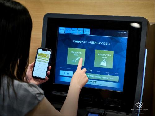 a woman holding a cell phone and pointing at a computer screen at Daiwa Roynet Hotel Oita in Oita