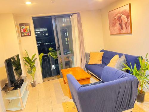 a living room with a blue couch and a tv at Authur's 2 bedrooms apartment, balcony, wifi, parking, cot, sunny, washing machine drier in Auckland
