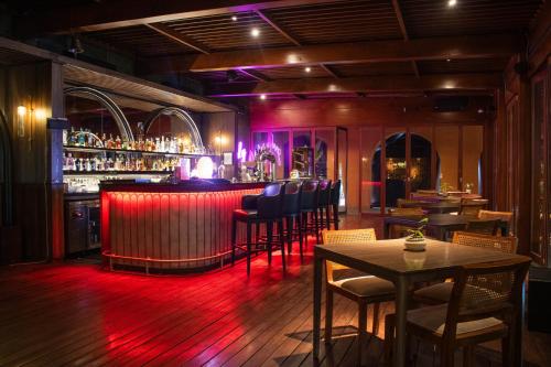 a bar with red lighting in a room with tables and chairs at ARTOTEL Suites Bianti Yogyakarta, CHSE Certified in Yogyakarta