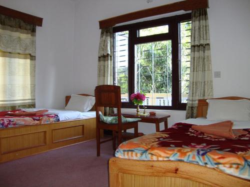 1 dormitorio con 2 camas, silla y ventana en New Summit Guest House, en Pokhara