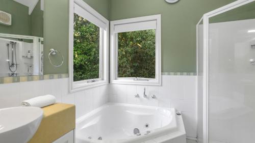 une salle de bain avec une baignoire et un lavabo et deux fenêtres dans l'établissement Little Plum Cottage, à Apollo Bay